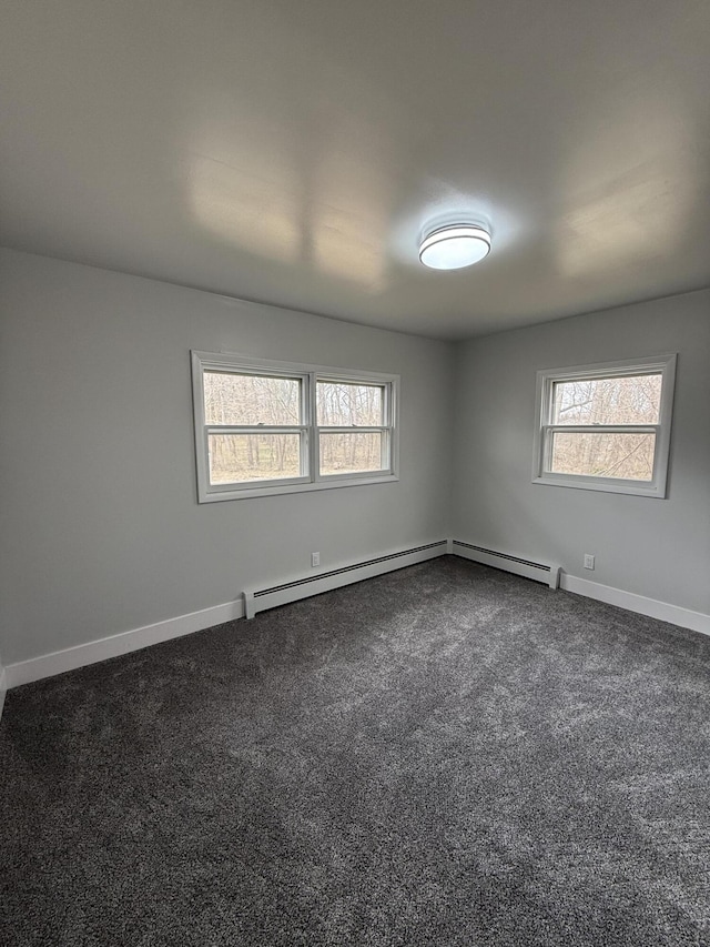 spare room featuring baseboards, dark carpet, a baseboard radiator, and a healthy amount of sunlight