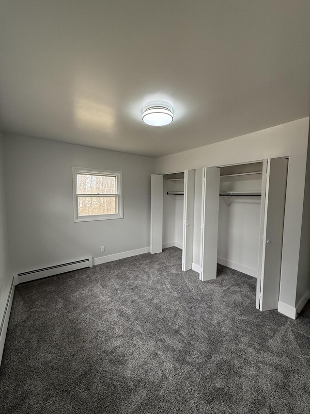 unfurnished bedroom with baseboards, dark carpet, a baseboard radiator, and multiple closets