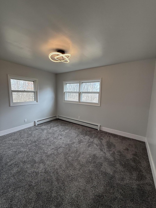 empty room featuring a baseboard heating unit, dark carpet, and baseboards