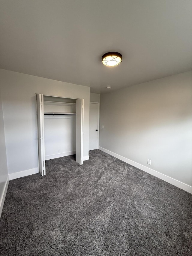 unfurnished bedroom featuring a closet, dark carpet, and baseboards