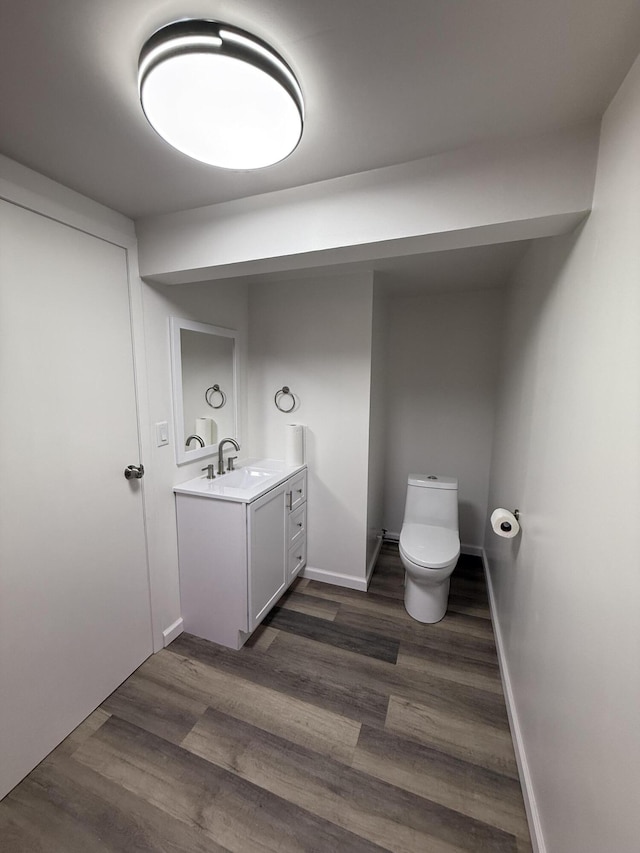 half bathroom featuring vanity, wood finished floors, toilet, and baseboards