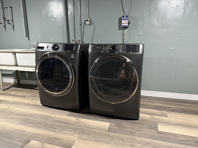 clothes washing area featuring washing machine and dryer, a sink, wood finished floors, laundry area, and baseboards