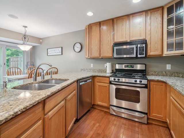 kitchen featuring light stone counters, stainless steel appliances, a sink, light wood-style floors, and decorative light fixtures