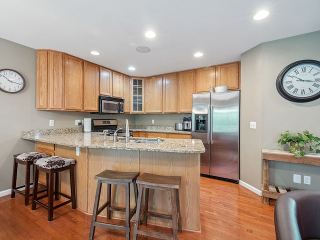 kitchen featuring appliances with stainless steel finishes, light wood-style floors, glass insert cabinets, light stone countertops, and a peninsula