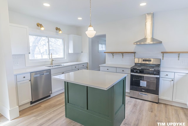 kitchen with stainless steel appliances, white cabinets, a sink, and wall chimney exhaust hood