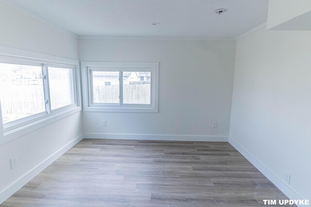 empty room with light wood-style flooring, baseboards, and crown molding