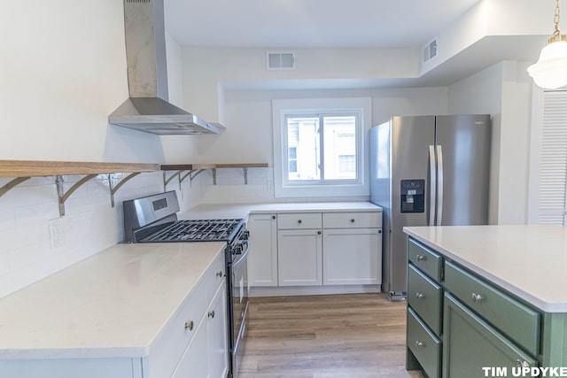 kitchen with visible vents, appliances with stainless steel finishes, wall chimney range hood, tasteful backsplash, and green cabinetry