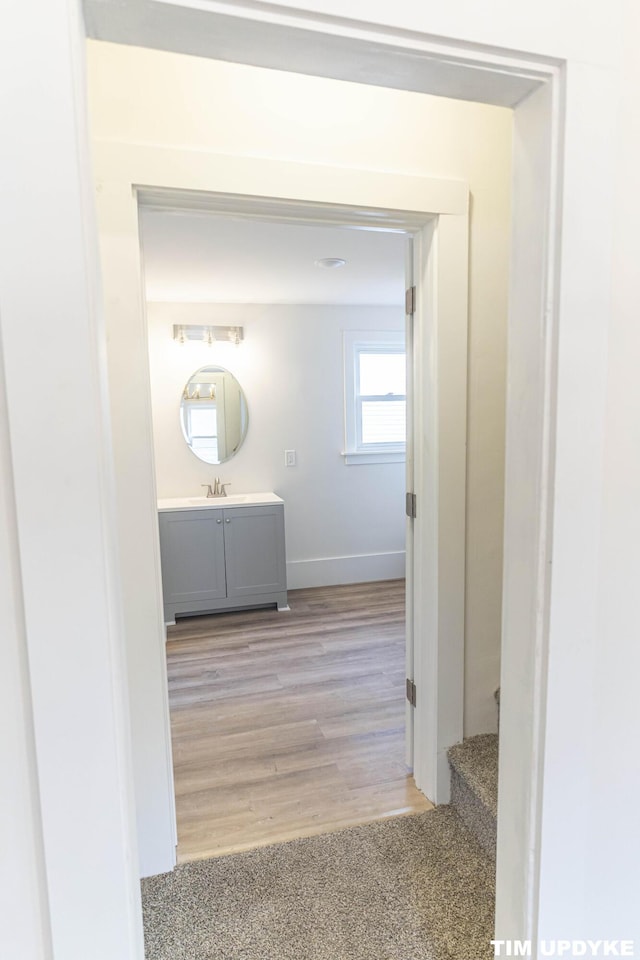 hall featuring light wood finished floors, baseboards, and a sink