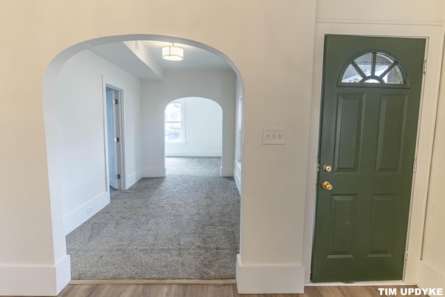 foyer entrance with carpet floors, arched walkways, baseboards, and wood finished floors