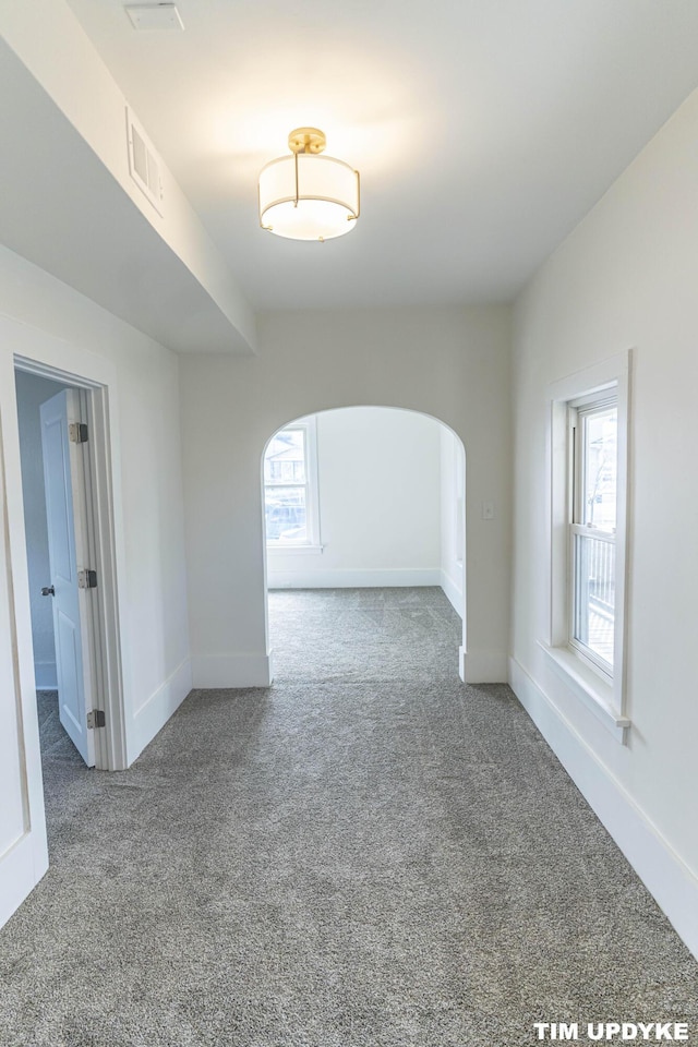 unfurnished room featuring arched walkways, carpet floors, visible vents, and baseboards