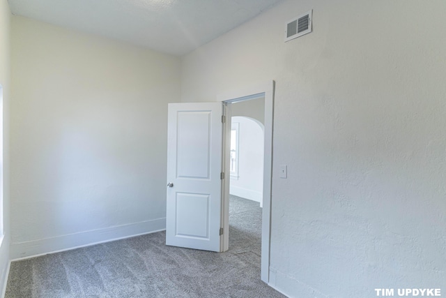 spare room with carpet floors, baseboards, visible vents, and arched walkways