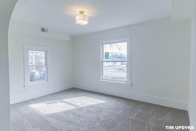 carpeted spare room featuring arched walkways, visible vents, and baseboards