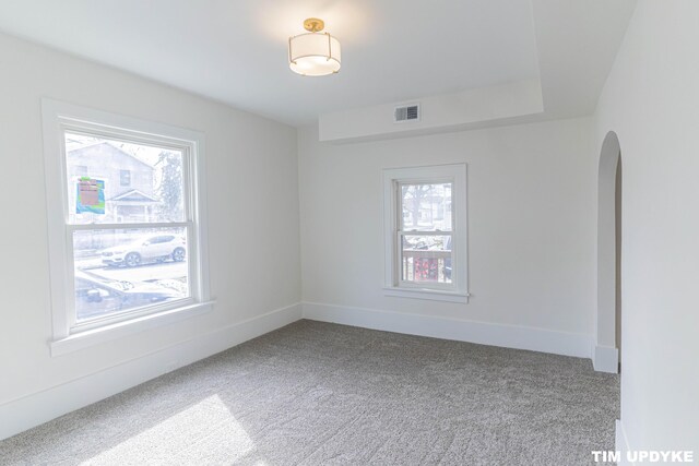 unfurnished room featuring carpet, visible vents, arched walkways, and baseboards