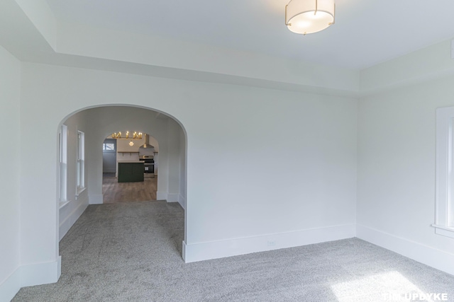 unfurnished room with carpet floors, baseboards, and arched walkways