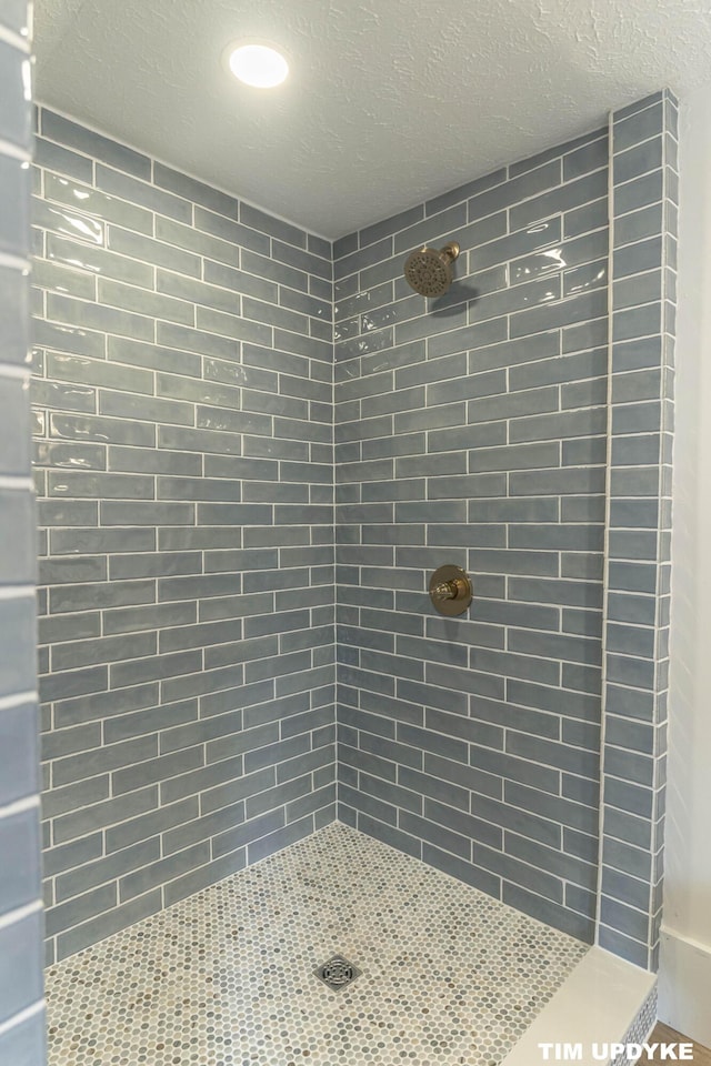 full bathroom featuring a textured ceiling and a tile shower