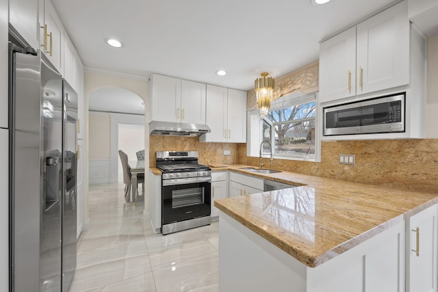 kitchen featuring tasteful backsplash, white cabinets, appliances with stainless steel finishes, under cabinet range hood, and a sink