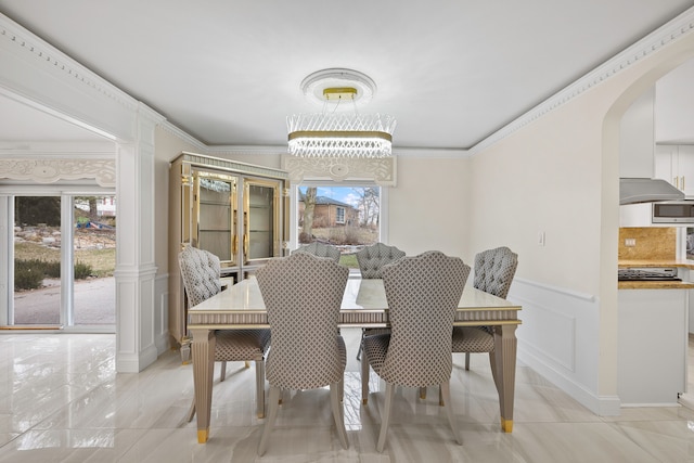 dining room featuring crown molding, arched walkways, a wainscoted wall, and a decorative wall