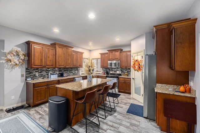 kitchen with a kitchen island, appliances with stainless steel finishes, brown cabinets, tasteful backsplash, and a kitchen bar