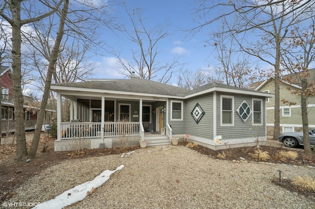 view of front facade with covered porch, roof with shingles, and gravel driveway