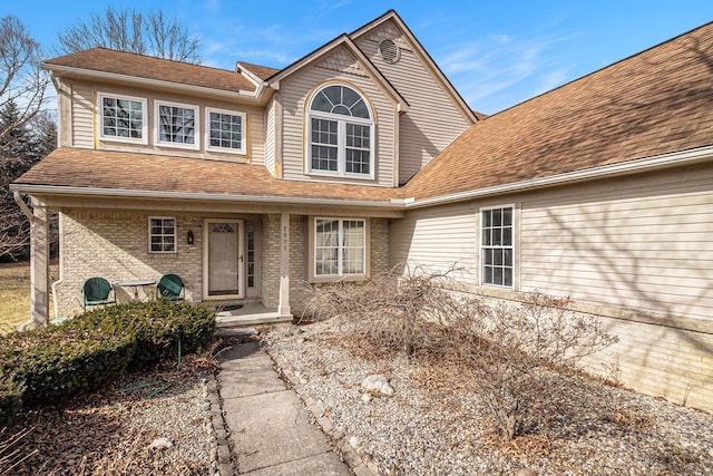 view of front of property featuring a porch, brick siding, and a shingled roof