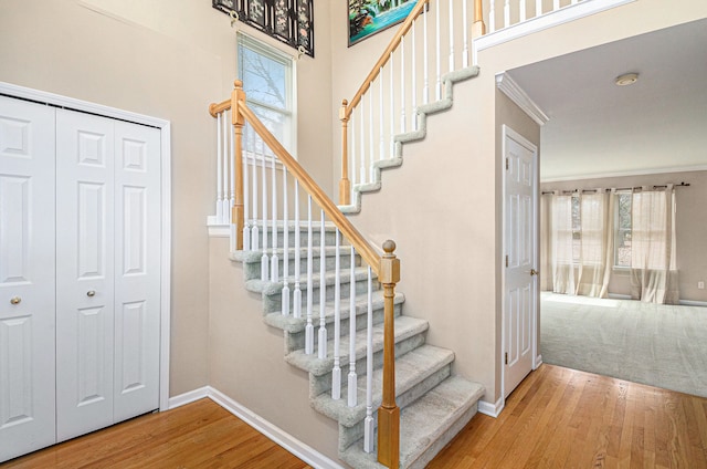 stairway with crown molding, a high ceiling, wood finished floors, and baseboards