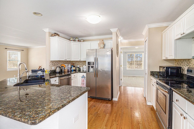 kitchen with stainless steel appliances, a peninsula, a sink, white cabinets, and crown molding