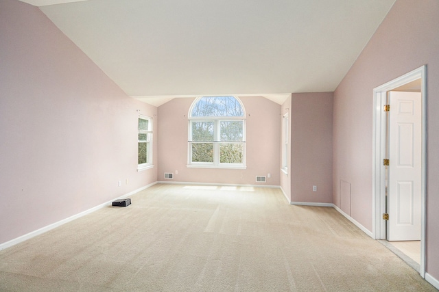 empty room featuring baseboards, visible vents, vaulted ceiling, and light colored carpet