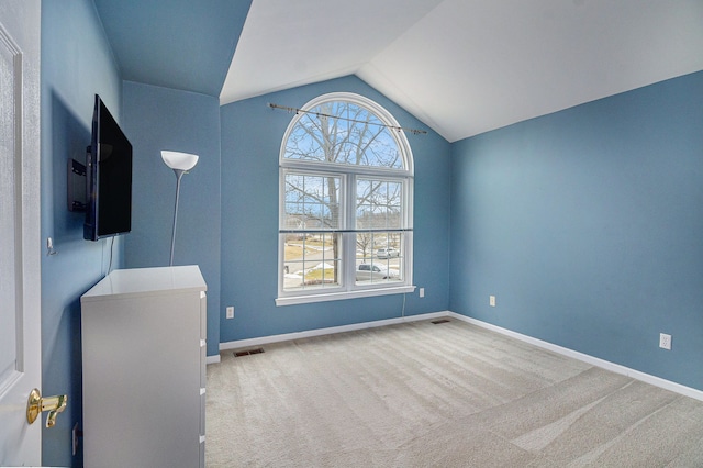 carpeted spare room with lofted ceiling, baseboards, and visible vents