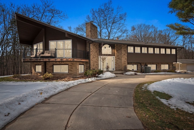 view of front of property featuring a balcony, a chimney, central AC unit, and brick siding