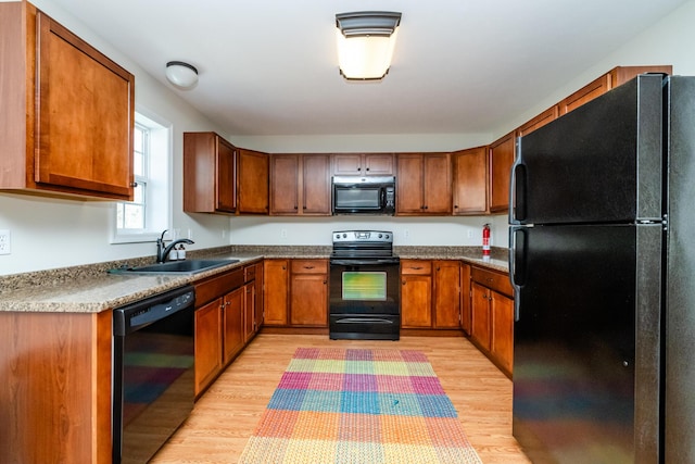 kitchen with brown cabinets, black appliances, light wood finished floors, and a sink