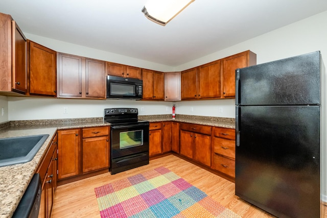 kitchen featuring light wood-style floors, brown cabinetry, a sink, and black appliances