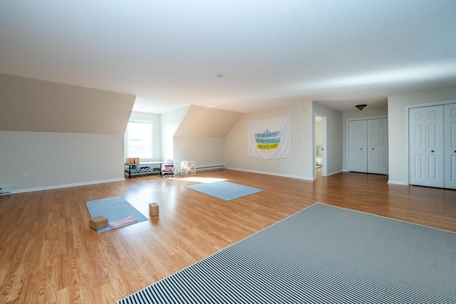 workout area featuring vaulted ceiling, a baseboard heating unit, wood finished floors, and baseboards