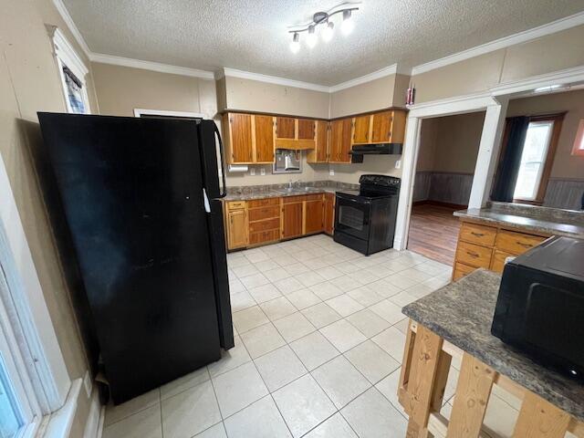 kitchen featuring brown cabinets, crown molding, under cabinet range hood, and black appliances