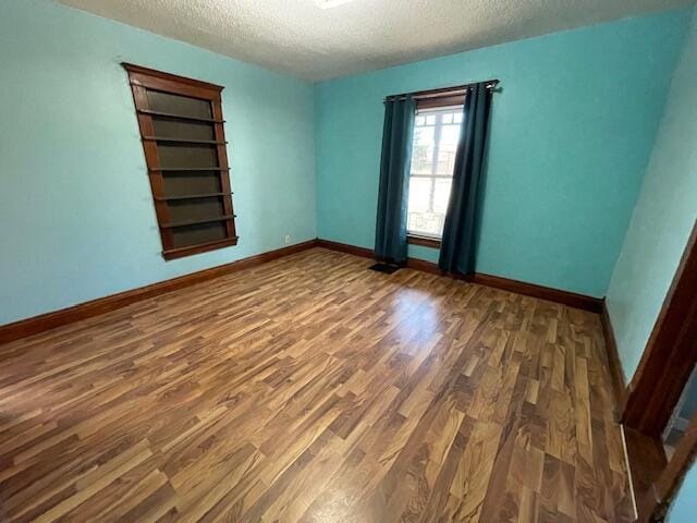 empty room with a textured ceiling, baseboards, and wood finished floors