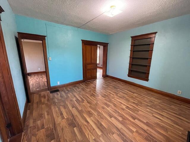 empty room featuring a textured ceiling, baseboards, and wood finished floors