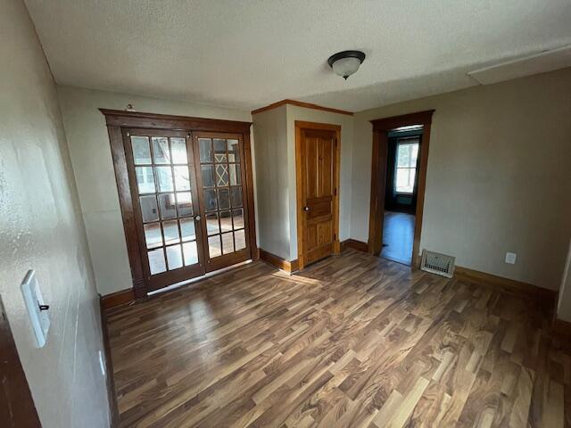 empty room featuring french doors, visible vents, a textured ceiling, wood finished floors, and baseboards