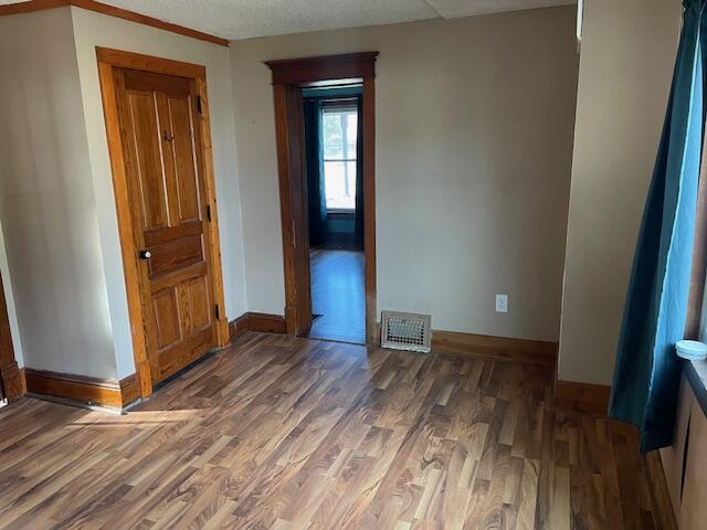 unfurnished room featuring a textured ceiling, wood finished floors, visible vents, and baseboards