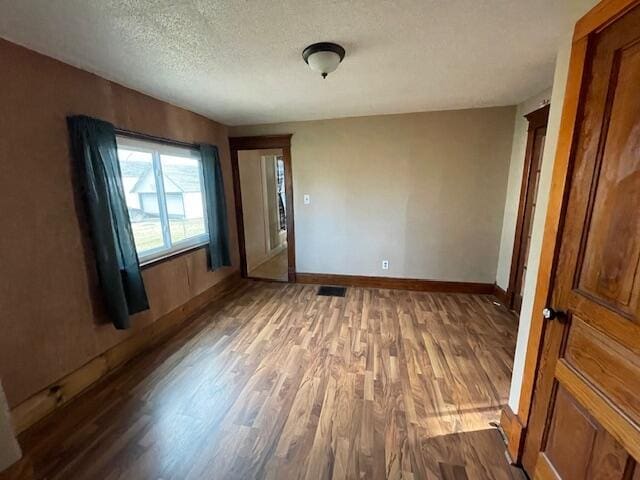 unfurnished room with a textured ceiling, wood finished floors, and baseboards