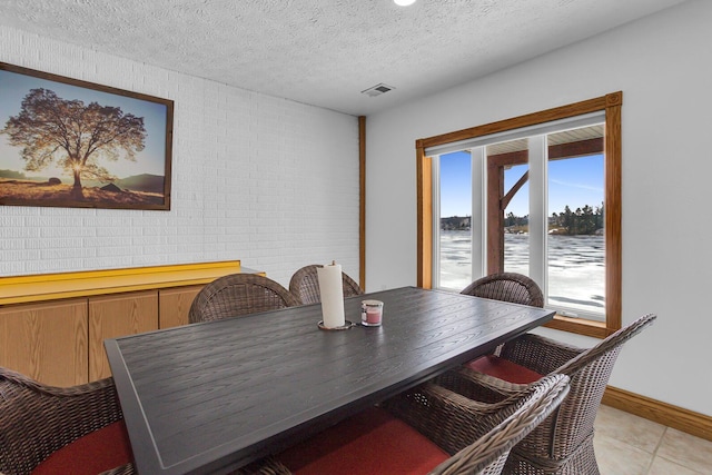 dining space with a water view, a textured ceiling, visible vents, baseboards, and light tile patterned floors
