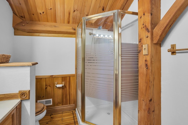 bathroom with wood walls, wainscoting, toilet, a stall shower, and wooden ceiling