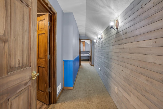 hallway with wooden walls, light colored carpet, and visible vents
