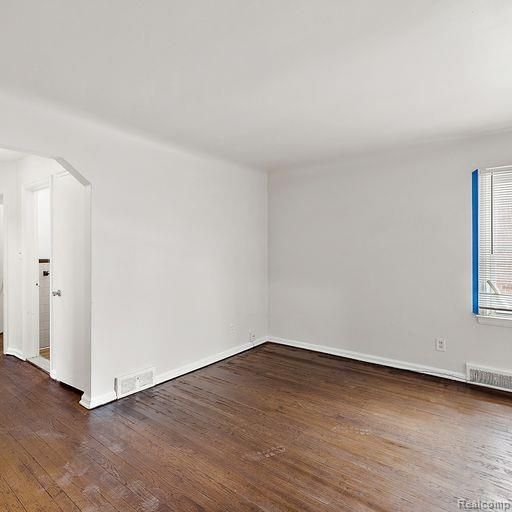 spare room with baseboards, visible vents, wood finished floors, and arched walkways