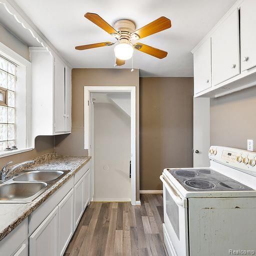 kitchen with a sink, a ceiling fan, white cabinetry, wood finished floors, and white electric range oven