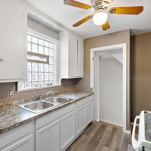 kitchen with light countertops, stove, a sink, white cabinets, and wood finished floors