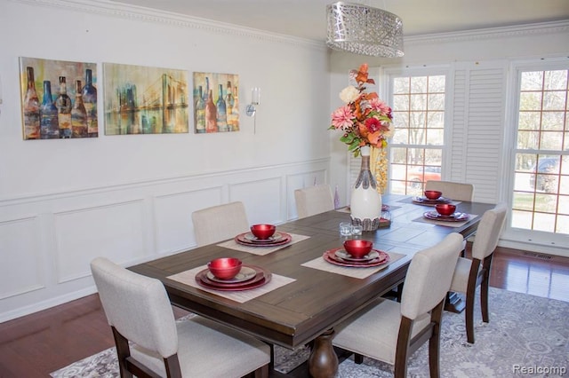 dining area featuring visible vents, wainscoting, ornamental molding, wood finished floors, and a decorative wall