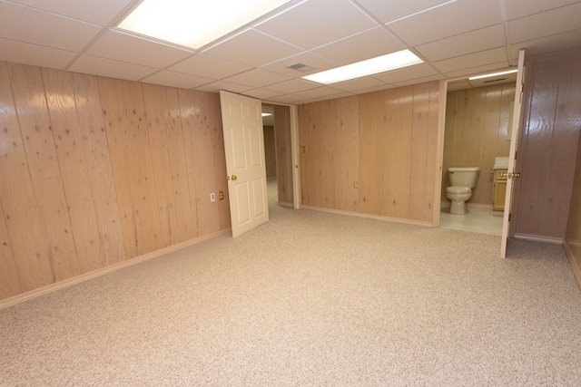 finished basement with a paneled ceiling, visible vents, wood walls, and baseboards