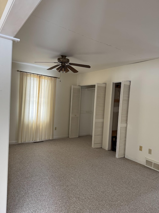 unfurnished bedroom with carpet floors, two closets, visible vents, ceiling fan, and baseboards