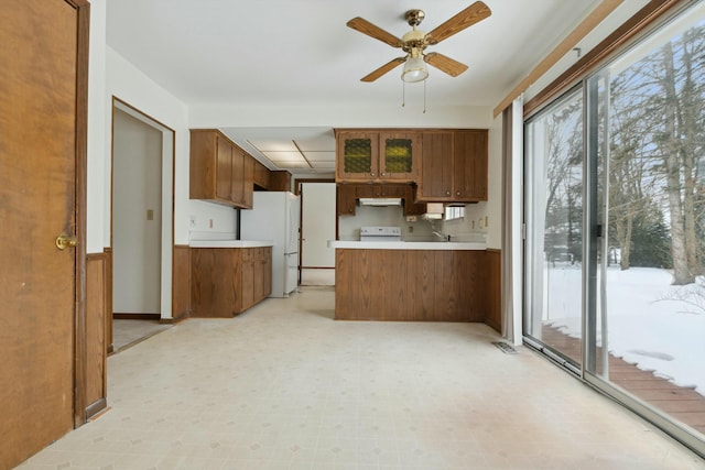 kitchen with a peninsula, light countertops, freestanding refrigerator, brown cabinets, and light floors