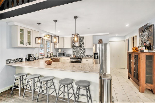 kitchen featuring a peninsula, a sink, appliances with stainless steel finishes, decorative backsplash, and a kitchen bar