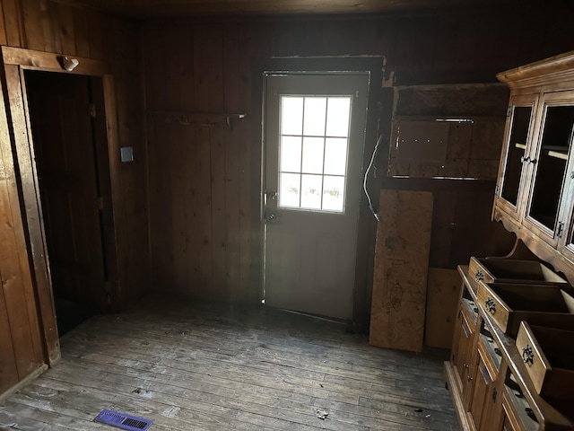 doorway with hardwood / wood-style floors, wood walls, and visible vents